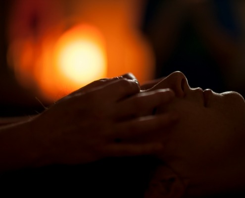 A shamanic healer's hands are gently placed over rthe eyes of a woman during a healing session