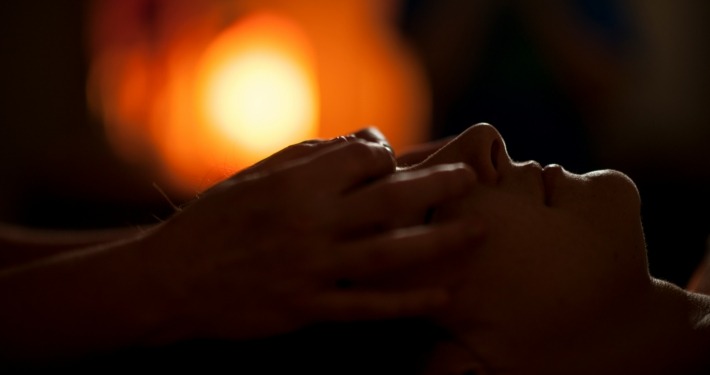 A shamanic healer's hands are gently placed over rthe eyes of a woman during a healing session