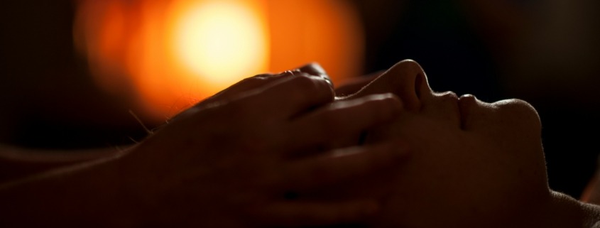 A shamanic healer's hands are gently placed over rthe eyes of a woman during a healing session