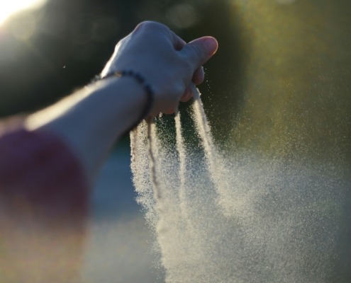 A woman's hand gradually taking her time to let go of sand from her finger tips