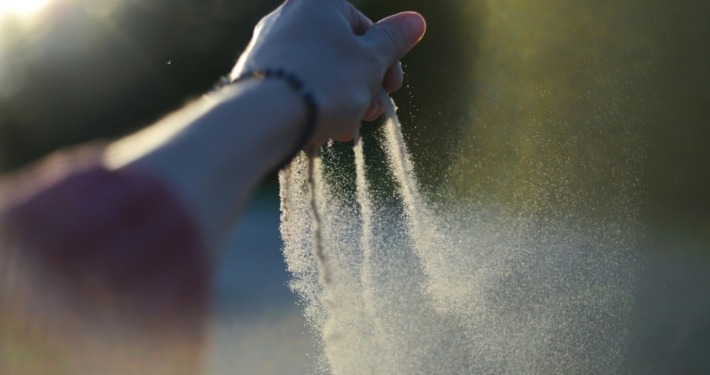 A woman's hand gradually taking her time to let go of sand from her finger tips