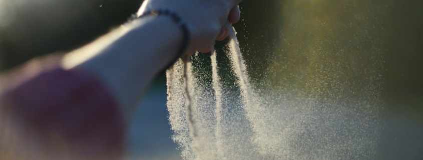 A woman's hand gradually taking her time to let go of sand from her finger tips