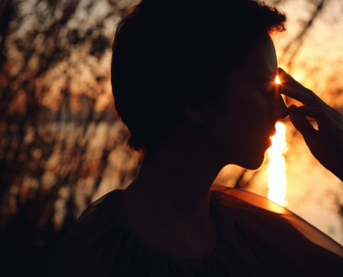 A woman holding her fingers to her third eye with the setting sun shining through her fingers